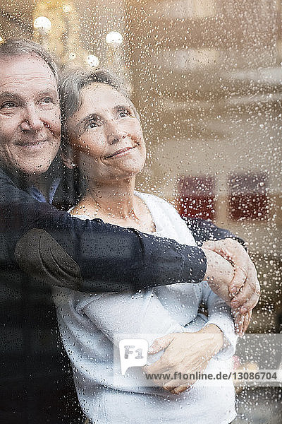 Liebevolles älteres Paar schaut durch nasses Fenster
