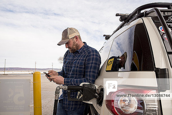 Mittelgroßer erwachsener Mann  der ein Smartphone benutzt  während er an der Tankstelle im Auto steht