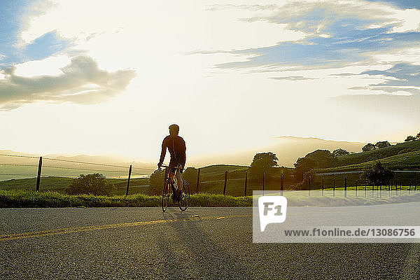 Young man cycling on street against cloudy sky