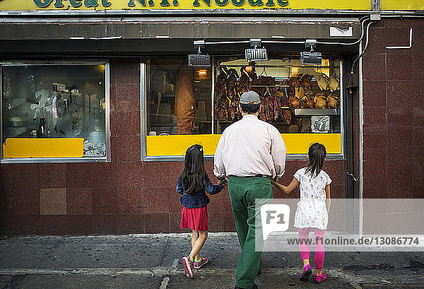 Großvater und Enkelkinder in voller Länge beim Anblick eines Restaurants in der Stadt