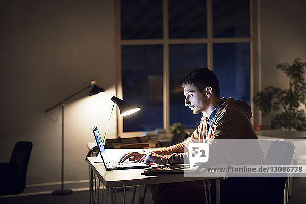 Seitenansicht eines Mannes  der nachts in der Bibliothek am Laptop lernt