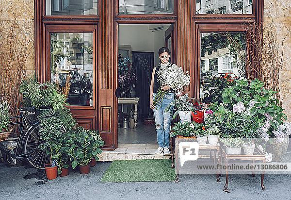 Female florist holding white flowers while standing entrance of shop
