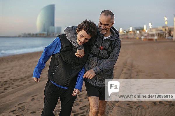 Verspielter Vater mit Arm um die Schulter des Sohnes geht gegen Hotel Vela am Strand