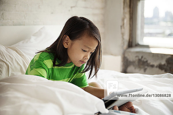 Lächelndes Mädchen benutzt Tablet-Computer  während es zu Hause im Bett liegt