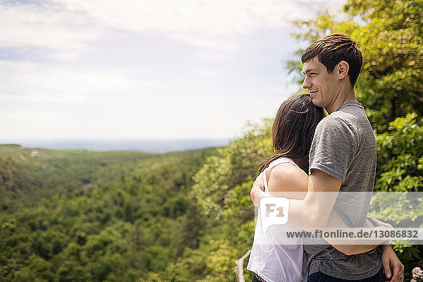 Side view of man embracing woman while standing against trees