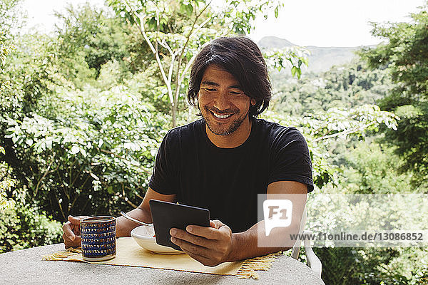 Lächelnder Mann benutzt Tablet-Computer  während er am Tisch im Hof sitzt