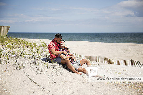 Homosexuelles Paar ruht sich am Strand gegen den Himmel