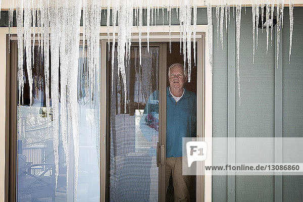 Man looking away while standing by widow at home during winter