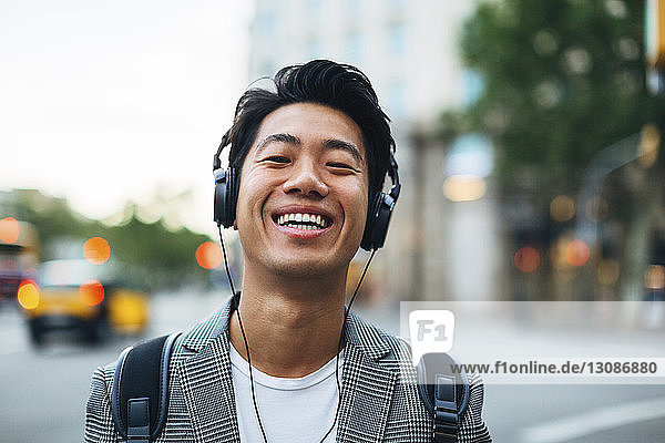 Portrait of happy businessman listening music in city