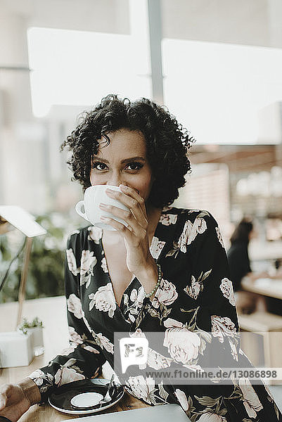 Portrait of woman drinking coffee while sitting at table in cafe