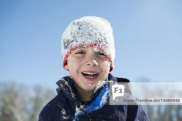 Porträt eines glücklichen  schneebedeckten Jungen  der vor klarem  blauem Himmel steht