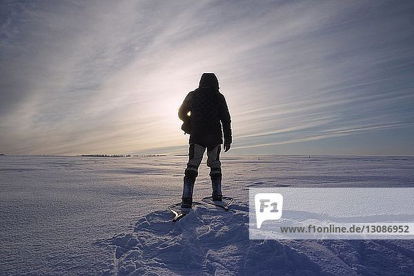Rear view of man standing on snow covered field against sky on sunny day