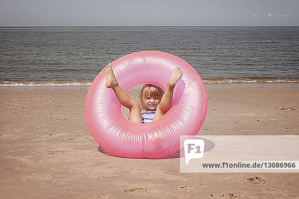 Porträt eines verspielten Mädchens mit aufblasbarem Ring am Strand