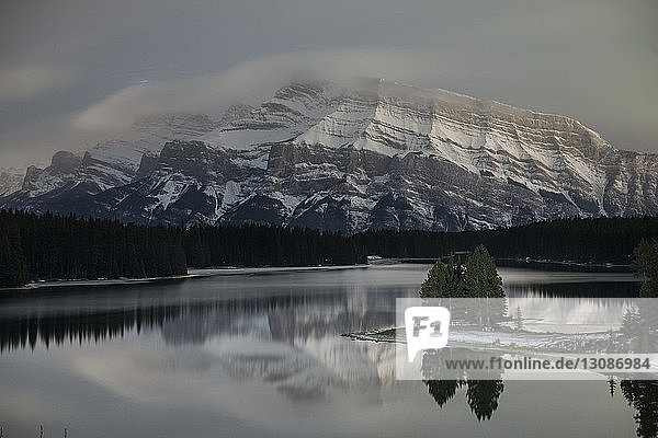 Szenenansicht von Two Jack Lake vor schneebedeckten Bergen in der Dämmerung