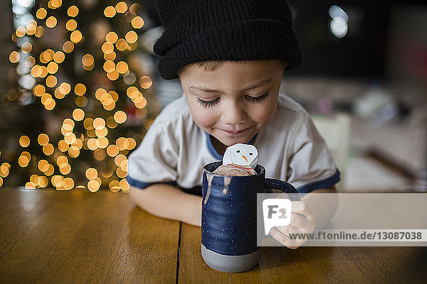Happy boy looking in cup with marshmallow snowman at home