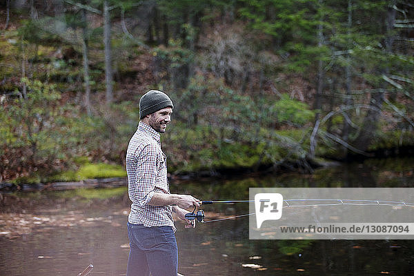Smiling man fishing in lake at forest