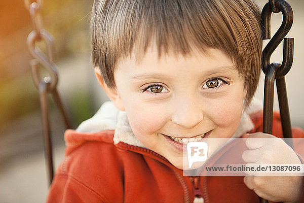 Porträt eines fröhlichen Jungen  der im Park auf der Schaukel spielt