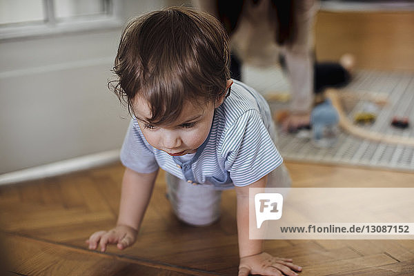 Süßer kleiner Junge krabbelt auf dem Harwood-Fußboden mit der Mutter im Hintergrund