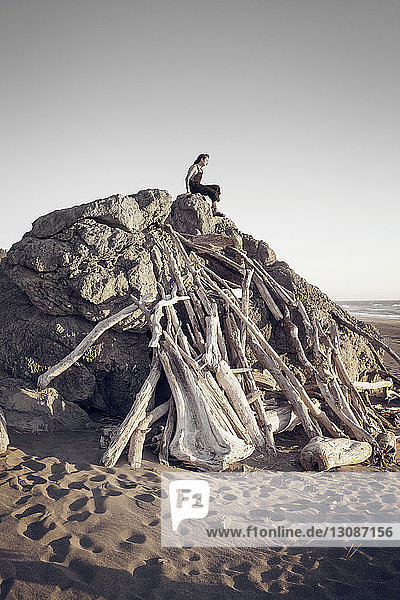Frau sitzt auf Felsformation am Strand vor klarem Himmel