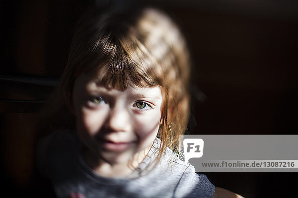Nahaufnahme-Porträt eines niedlichen Mädchens  das an einem sonnigen Tag in einem dunklen Raum steht
