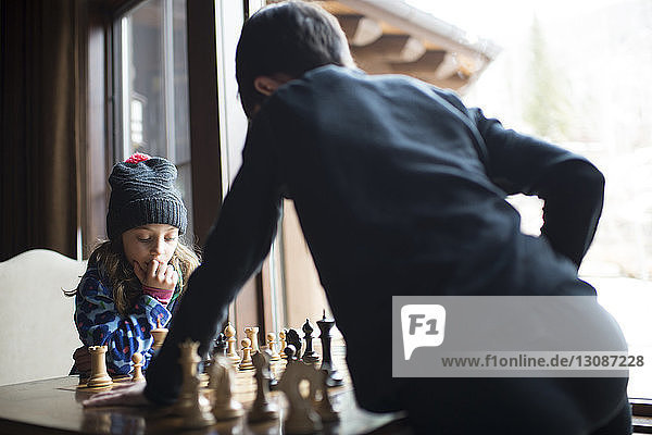 Geschwister spielen Schach  während sie zu Hause am Fenster stehen