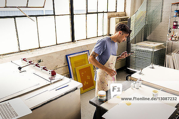 Worker using phone while standing at workbench in workshop