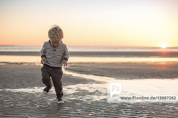 Junge in voller Länge  der bei Sonnenuntergang am Strand gegen den Himmel läuft