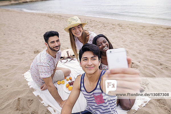 Friends taking selfie while enjoying picnic on beach