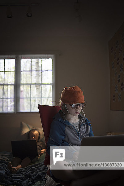 Junge benutzt Laptop-Computer  während er zu Hause auf einem Stuhl sitzt