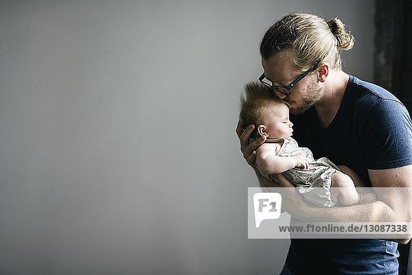 Vater küsst schlafende Tochter  während er sie vor grauem Hintergrund trägt