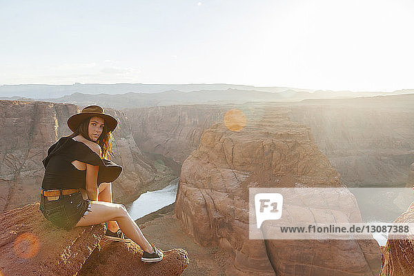 Ganzflächiges Porträt einer auf einem Felsen sitzenden jungen Frau bei Horseshoe Bend an einem sonnigen Tag in der Wüste