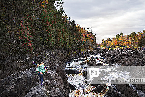 Rear view of woman walking over rocks by river at Jay Cooke State Park