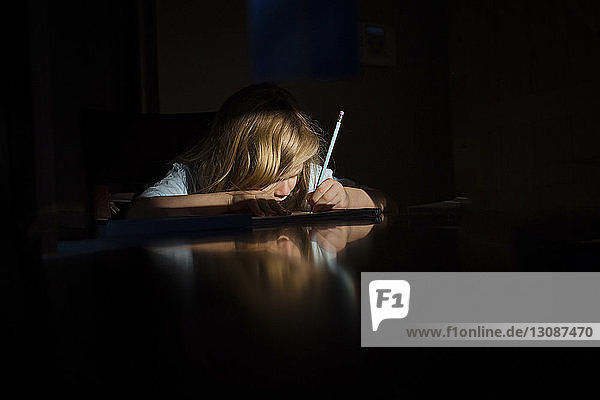 Mädchen schreibt Hausaufgaben  während sie in der Dunkelkammer des Hauses am Tisch sitzt