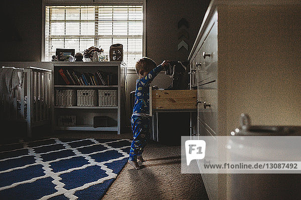 Seitenansicht eines kleinen Jungen  der zu Hause Kleidung in einer Schublade sucht