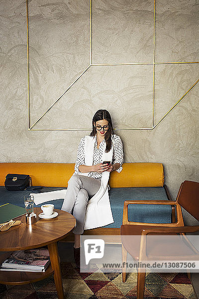 Smiling businesswoman using smart phone while sitting on sofa in hotel lobby