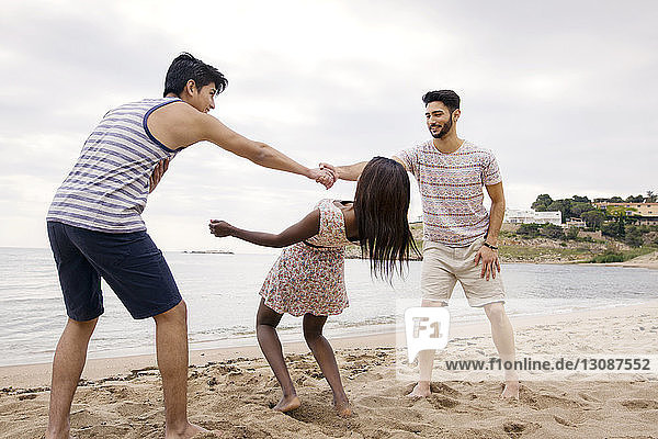 Woman passing under men's arms while playing on beach