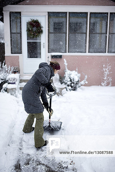 Frau schaufelt Schnee vor dem Haus