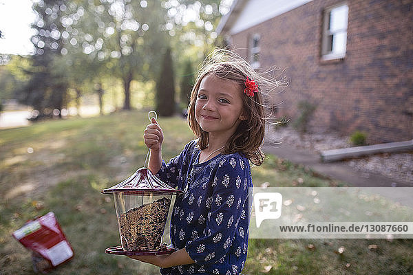 Porträt eines lächelnden Mädchens  das auf einem Feld im Hof steht und ein Futterhäuschen hält