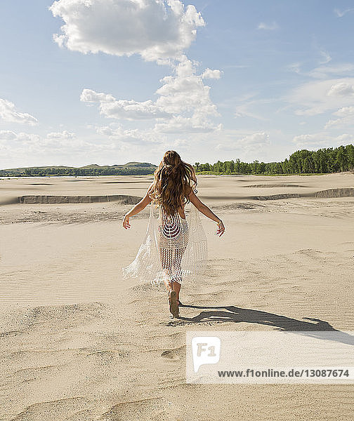 Rückansicht einer jungen Frau im Bikini  die auf Sand am Strand gegen den Himmel läuft