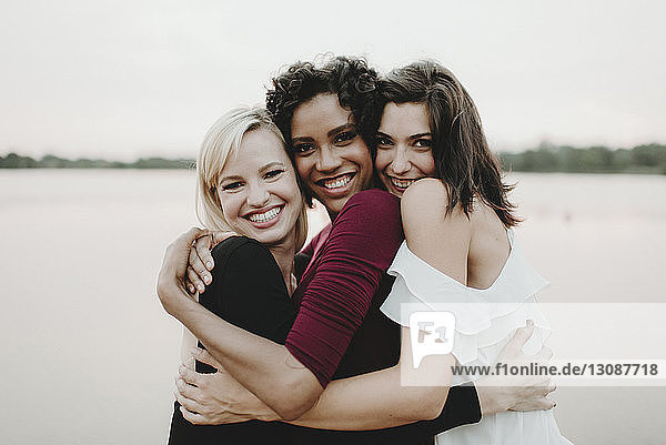 Portrait of cheerful female friends embracing against lake