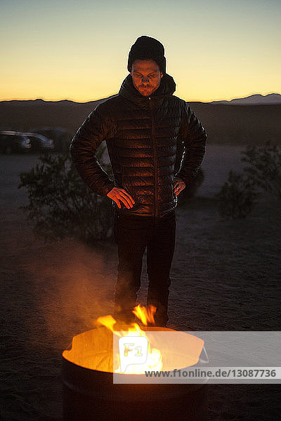 Mann steht am Lagerfeuer bei Sonnenuntergang