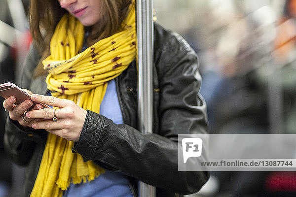 Mittelsektion einer Frau  die im Zug stehend ein Mobiltelefon benutzt