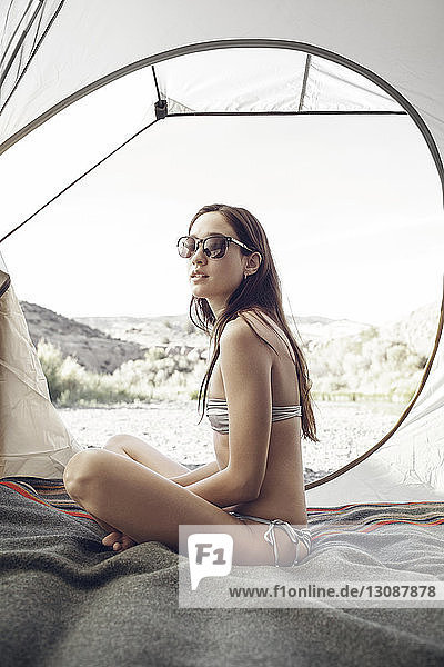 Seitenansicht einer sinnlichen Frau mit Sonnenbrille  die sich im Zelt entspannt