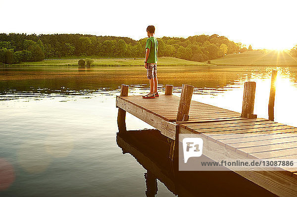 Boy standing on jetty over lake during sunny day