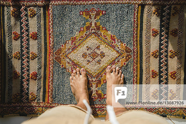 Niedriger Teil des Mannes auf traditionellem Teppich stehend
