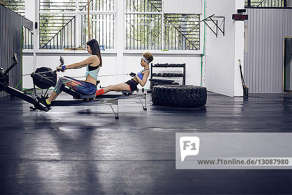 Seitenansicht von Sportlerinnen  die im Fitnessstudio auf einem Rudergerät trainieren