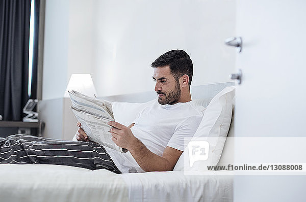 Mann liest Zeitung  während er sich auf dem Bett im Hotelzimmer entspannt