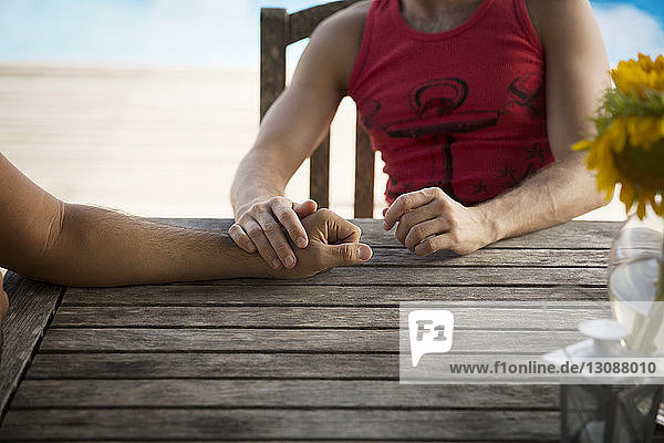 Ausgeschnittenes Bild eines homosexuellen Paares  das sich an einem Holztisch im Resort ausruht