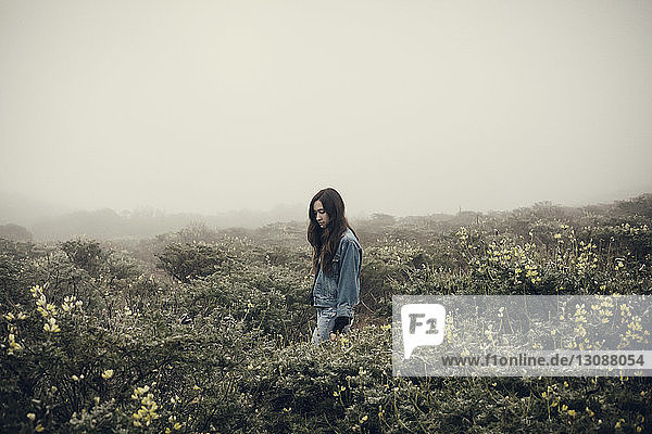Woman standing amidst flowering plants during foggy weather