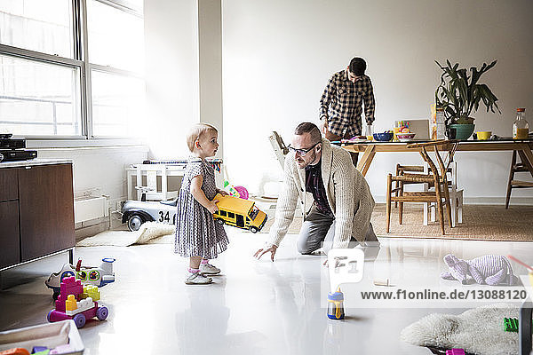 Vater spielt mit der Tochter  der Partner arbeitet am Tisch im hell erleuchteten Wohnzimmer